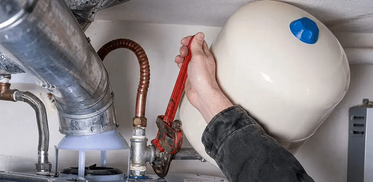 Water heater repair technician tightening plumbing connections near a tank unit in Jackson, MS